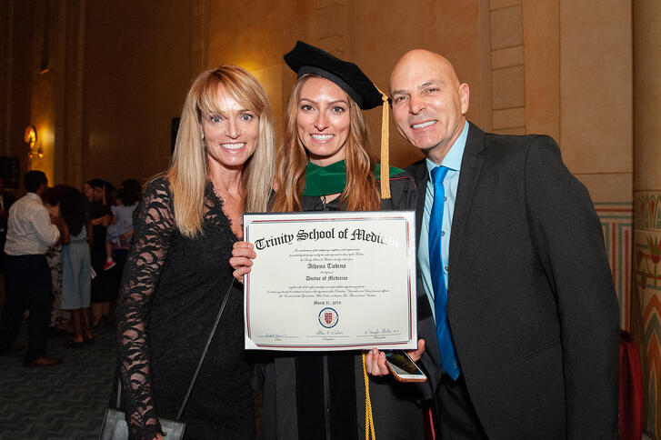 Trinity Medical School graduate holding up diploma