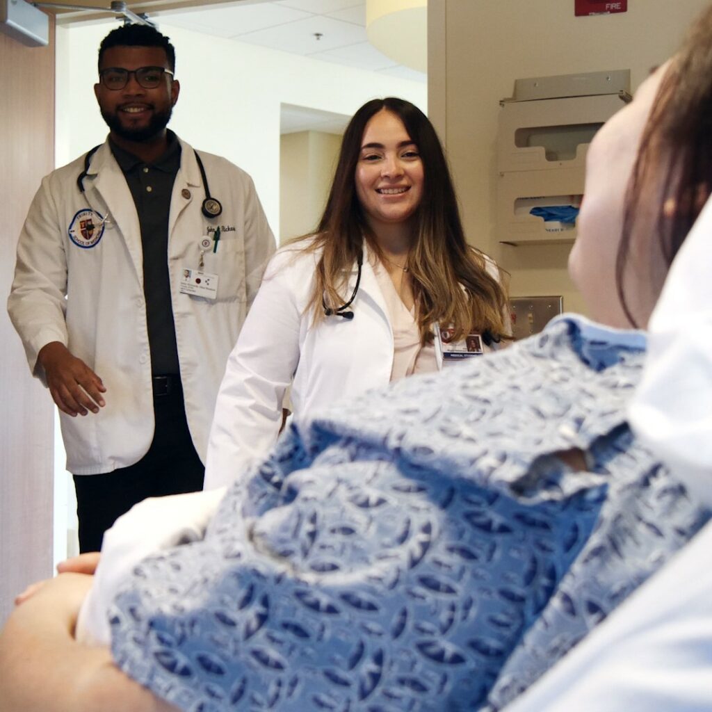 Two medical school students smiling while participating in clinical rotations for med school