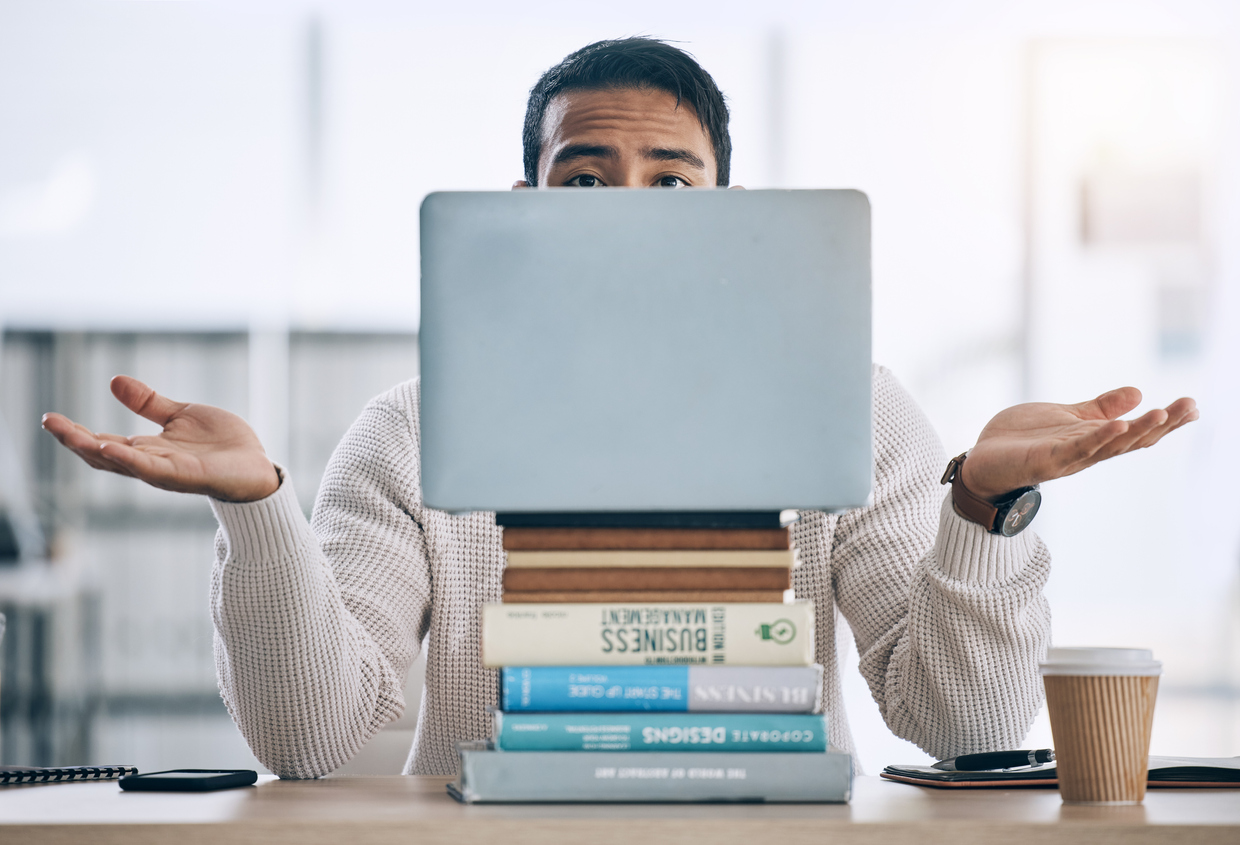 Confused college student shrugs with stack of books and laptop